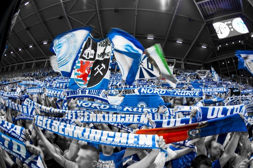Schalker Fans in der Kurve mit erhobenen Schals und Fahnen